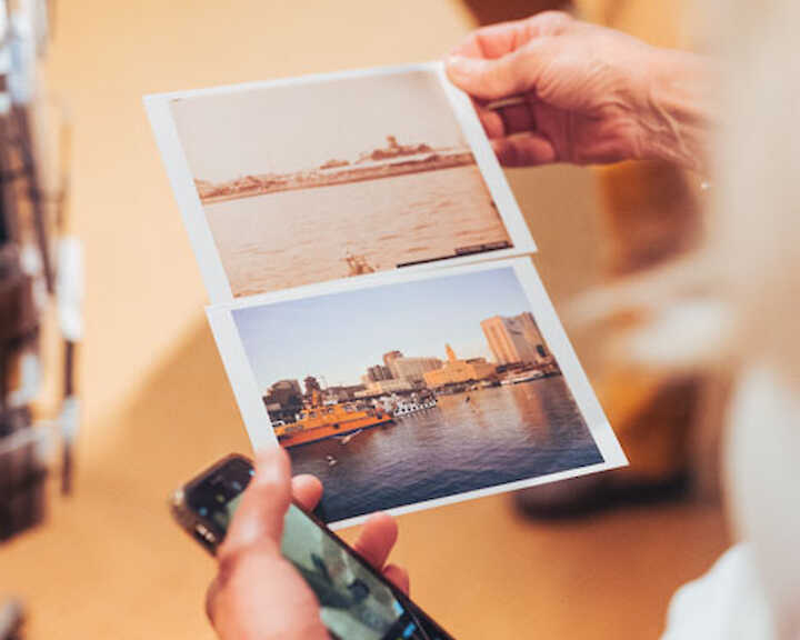 Detail: Hände halten zwei Postkarten nebeneinander. Ein historisches und ein modernes Motiv einer Stadt.  © buerofuerkunstdokumentation