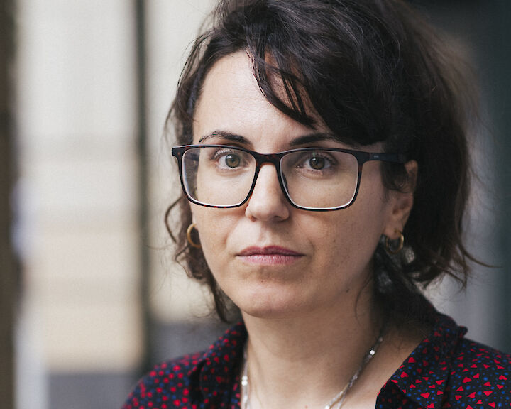 Portrait von Elena Efeoglou. Sie hat lange dunkle Haare und trägt eine Brille und eine dunkle Bluse mit roten Punkten.  © buerofuerkunstdokumentation