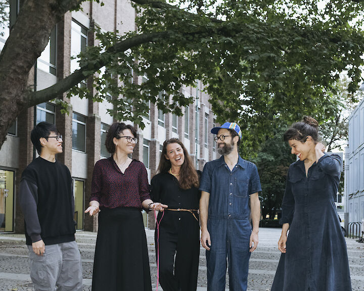 The 5 Artist Meets Artist artists stand smiling on a cobbled street under green trees. Elena Efeoglou has a dachshund on a leash.  © Silviu Guiman